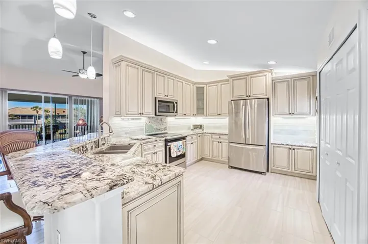 Kitchen with cream cabinetry, stainless steel appliances, a peninsula, hanging light fixtures, and light stone countertops