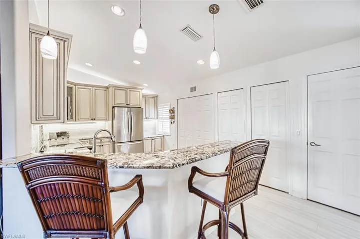 Kitchen featuring cream cabinetry, a breakfast bar, light stone countertops, decorative light fixtures, and freestanding refrigerator