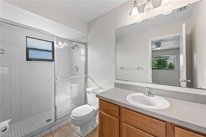 Bathroom featuring ceiling fan, vanity, toilet, walk in shower, and tile patterned flooring