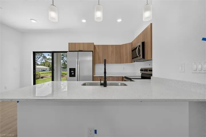 Kitchen featuring a large light-toned countertop, stainless steel appliances, wood-finish cabinetry, and recessed lighting