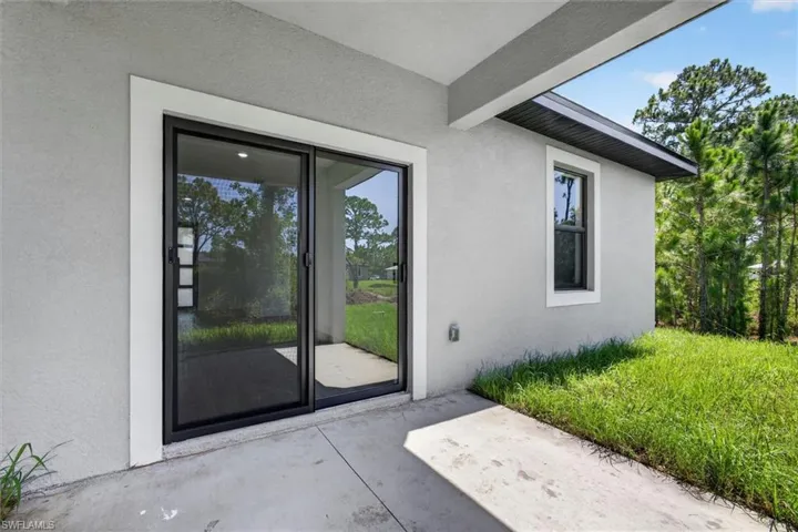 Outdoor patio space featuring a concrete surface, sliding glass doors, a single window with dark framing, a light-colored stucco exterior, and a black soffit