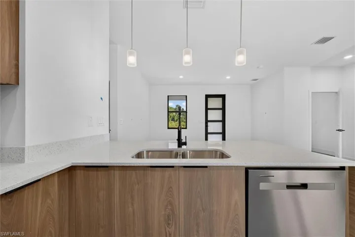 Kitchen island featuring a stainless steel sink with a black faucet, light wood-finish cabinetry, a stainless steel dishwasher, and light speckled countertops
