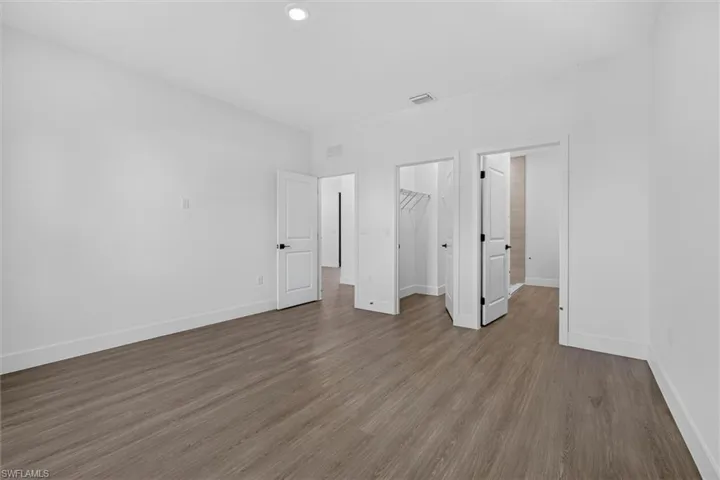 Spacious room featuring wood-finish flooring, white baseboards, and bright white walls