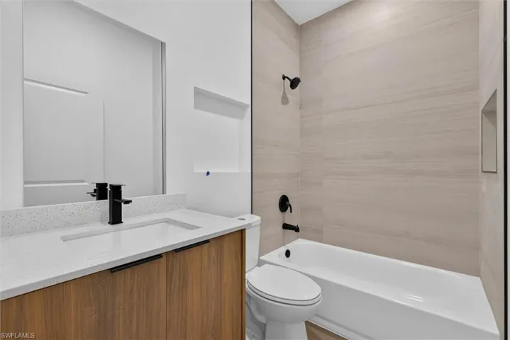 Bathroom featuring a wood-finish vanity with a white countertop, an undermount sink, and a matte black faucet