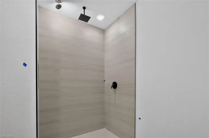 Shower enclosure featuring large format light-toned tile, a matte black rain shower head, and a coordinating matte black control knob