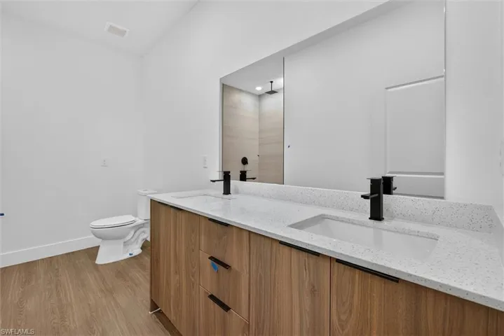Dual vanity featuring wood-finish cabinetry, white solid surface countertops, integrated sinks, and matte black fixtures