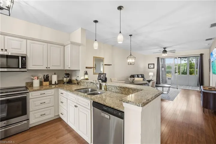 Kitchen with stainless steel appliances, light stone countertops, open floor plan, a peninsula, and pendant lighting