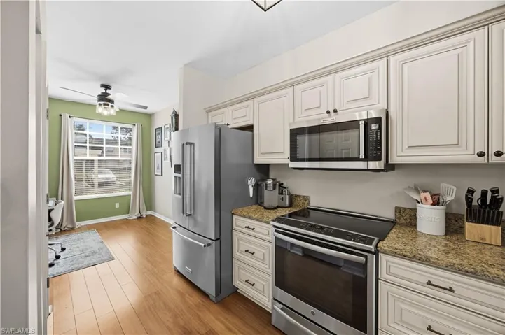 Kitchen with stainless steel appliances, dark stone countertops, ceiling fan, and light wood-style floors
