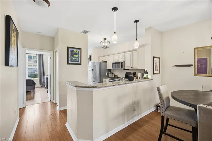 Kitchen featuring light wood finished floors, dark stone countertops, a peninsula, and stainless steel microwave