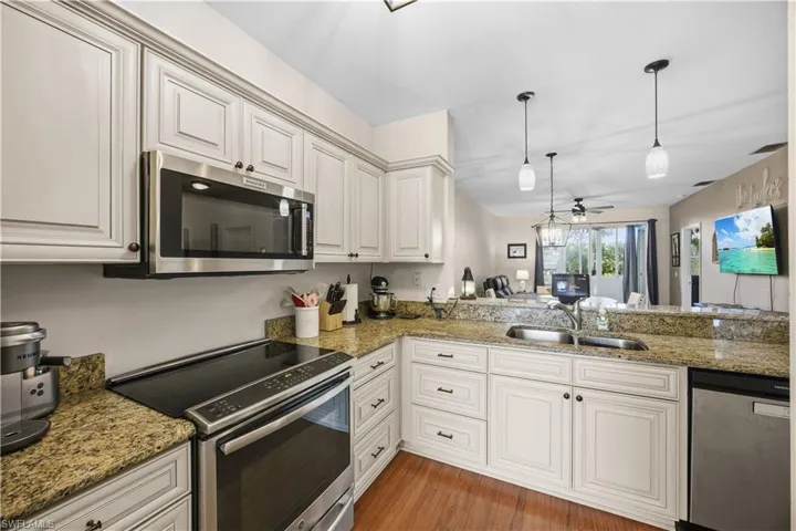 Kitchen with stainless steel appliances, decorative light fixtures, light stone counters, a ceiling fan, and a peninsula