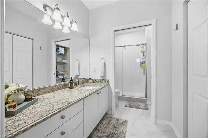 Bathroom featuring a shower stall, vanity, light marble finish floors, and a spacious closet