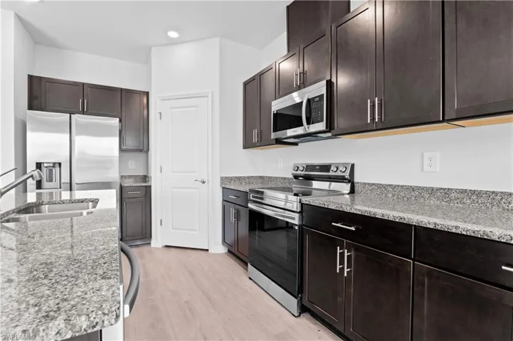 Kitchen with stainless steel appliances, dark brown cabinets, light wood-style floors, light stone counters, and recessed lighting