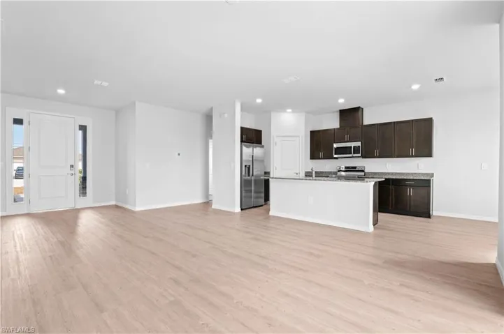 Kitchen with open floor plan, dark brown cabinets, stainless steel appliances, light wood-type flooring, and recessed lighting