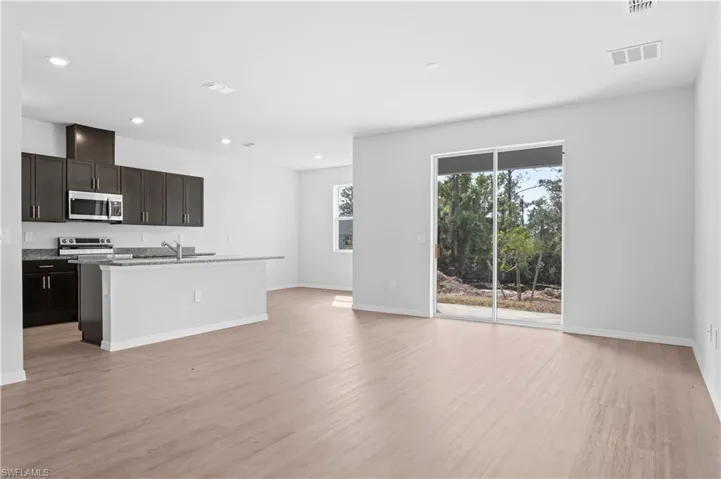 Kitchen with dark brown cabinetry, a center island with sink, open floor plan, appliances with stainless steel finishes, and recessed lighting