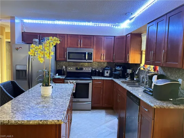 Kitchen with reddish brown cabinets, light tile patterned floors, tasteful backsplash, appliances with stainless steel finishes, and a sink