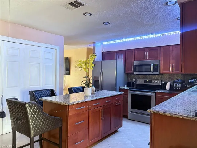 Kitchen featuring light tile patterned floors, stainless steel appliances, visible vents, decorative backsplash, and dark brown cabinets