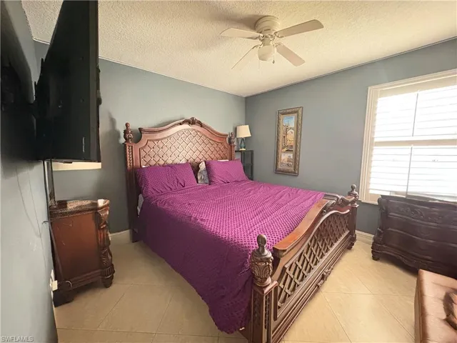 Tiled bedroom with ceiling fan, baseboards, and a textured ceiling