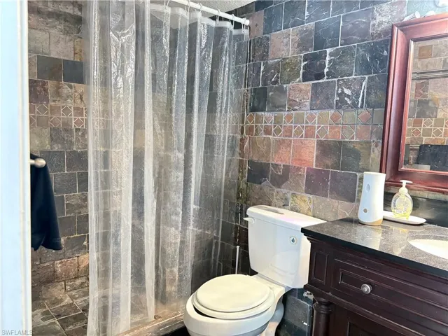 Bathroom with toilet, tile walls, tiled shower, and vanity