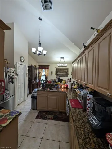Kitchen with lofted ceiling, light tile patterned floors, a peninsula, freestanding refrigerator, and decorative light fixtures