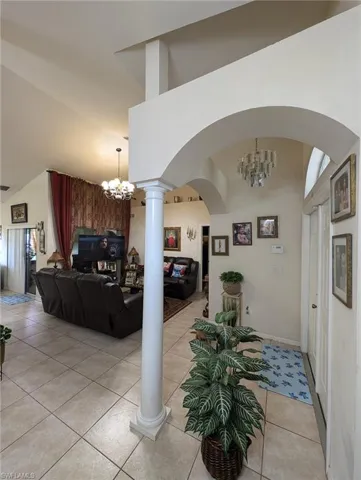Corridor featuring a chandelier, light tile patterned floors, arched walkways, high vaulted ceiling, and ornate columns