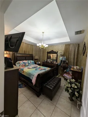 Bedroom with a chandelier, light tile patterned flooring, a raised ceiling, and wallpapered walls