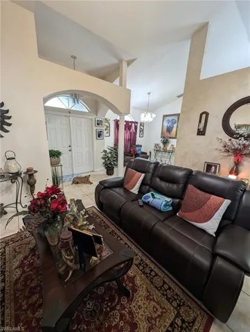 Living room with tile patterned flooring, a chandelier, ornate columns, arched walkways, and high vaulted ceiling