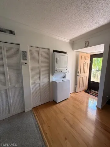 Laundry area with stacked washing machine and dryer, a textured ceiling, light wood-style floors, and ornamental molding