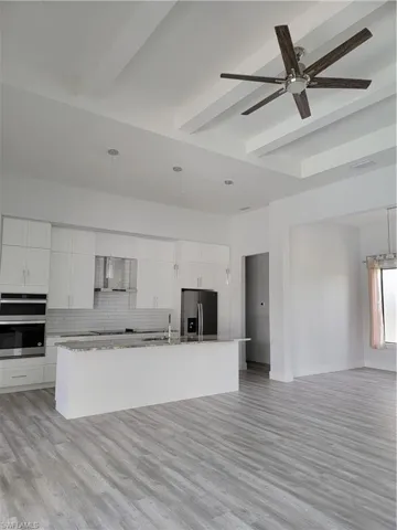 Kitchen featuring refrigerator, decorative backsplash, light hardwood / wood-style flooring, and a center island with sink