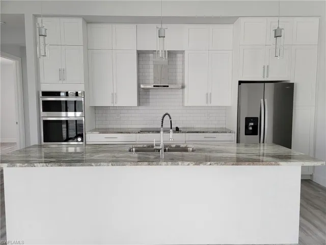 Kitchen featuring an island with sink, light stone countertops, light wood-type flooring, white cabinetry, and appliances with stainless steel finishes
