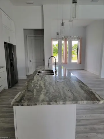 Kitchen with hardwood / wood-style flooring, sink, refrigerator, decorative light fixtures, and white cabinets