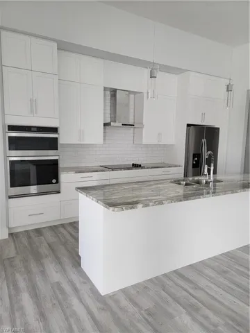 Kitchen with white cabinetry, light stone counters, decorative light fixtures, and stovetop