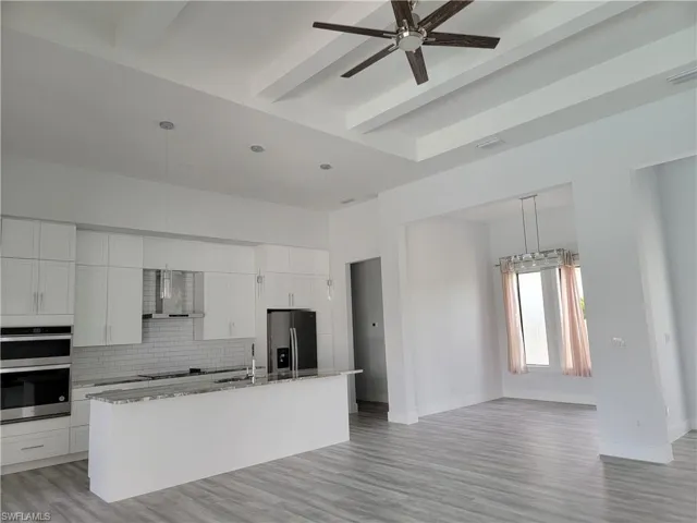 Kitchen with beam ceiling, tasteful backsplash, stainless steel appliances, and an island with sink