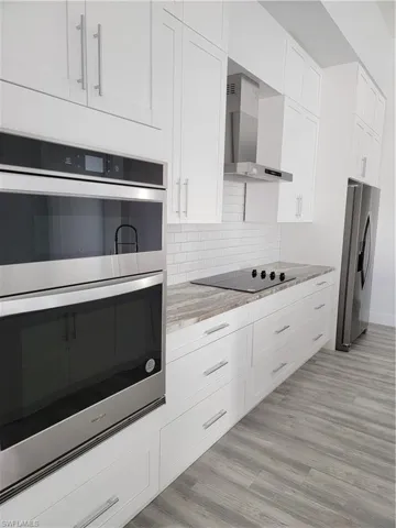 Kitchen with extractor fan, white cabinetry, refrigerator, light stone counters, and stainless steel double oven