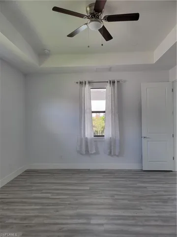 Empty room featuring a tray ceiling, wood-type flooring, and ceiling fan