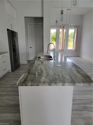 Kitchen with fridge, hanging light fixtures, a center island with sink, sink, and white cabinetry