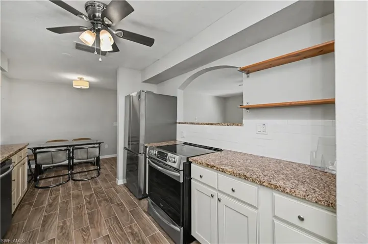Kitchen with open shelves, stainless steel appliances, wood finish floors, and light stone counters