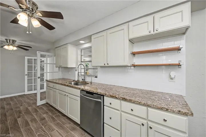 Kitchen featuring light stone countertops, stainless steel dishwasher, and white cabinetry