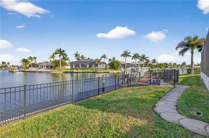 View of yard fully fenced, puppy pickets, walkway leading to dock with sitting area, electric, and boat lift with 2 new motors (2025), and wide water intersecting canal views