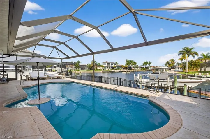 Heated swimming pool with cocktail seating & umbrella, boat lift, a dock, a wide water canal view, & gulf access