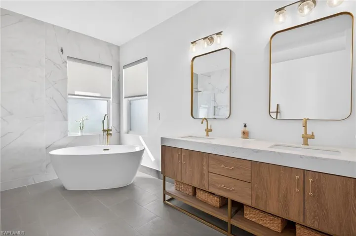 Primary bathroom featuring double vanity, a freestanding tub, and 36' tile walls