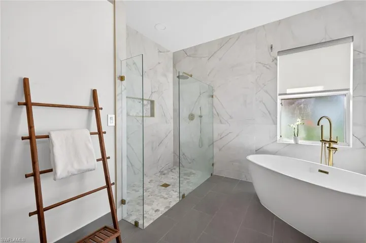 Primary bathroom featuring large separate shower with marble flooring, freestanding tub and tile plank flooring