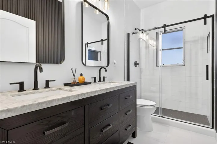 Full updated guest bathroom featuring double vanity, a stall shower, and light tile patterned floors