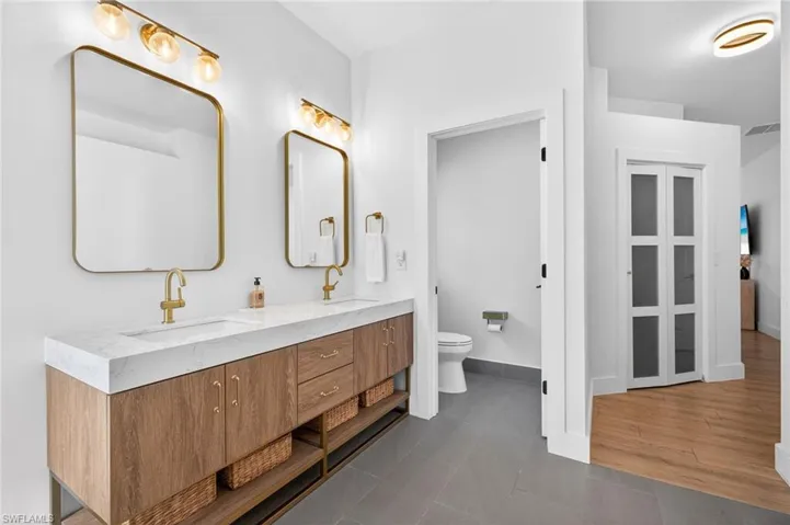 Primary suite with spa-like bathroom featuring double vanity, tile plank floors, private toilet