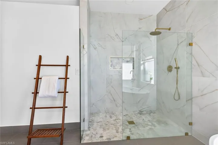Primary bathroom featuring a rain-shower and wand, 36' tile surround, marble shower floor and cubby