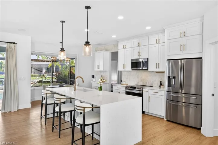 Renovated Kitchen with stainless steel appliances, white cabinets, light stone quartz countertops, and light wood-style LVP flooring