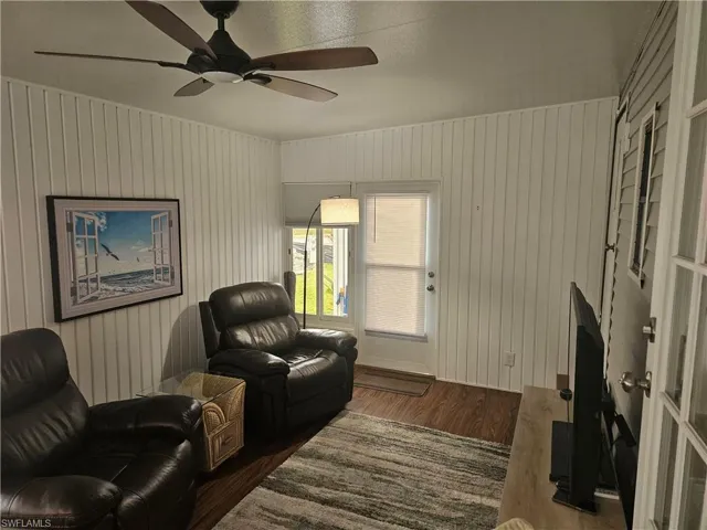 Living room with dark hardwood / wood-style floors, ceiling fan, and wooden walls