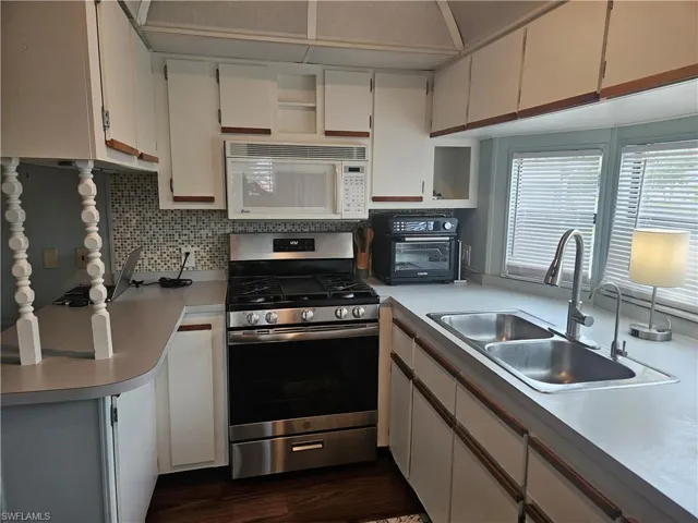 Kitchen with backsplash, white cabinets, sink, and stainless steel stove