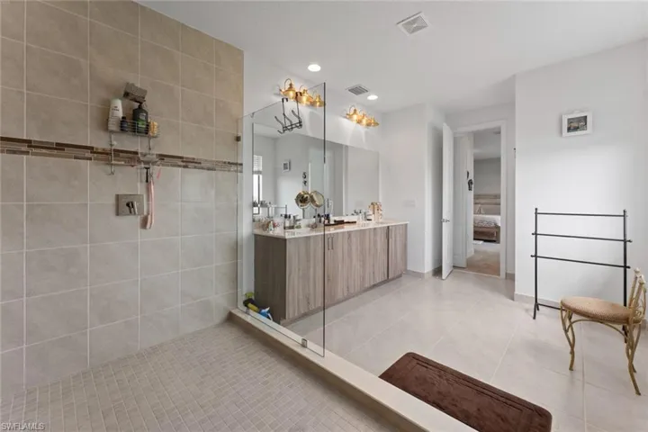 Ensuite bathroom featuring double vanity, visible vents, tiled shower, tile patterned floors, and recessed lighting
