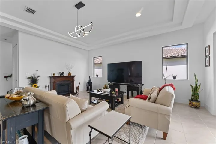 Living area with light tile patterned floors, baseboards, visible vents, a raised ceiling, and a fireplace