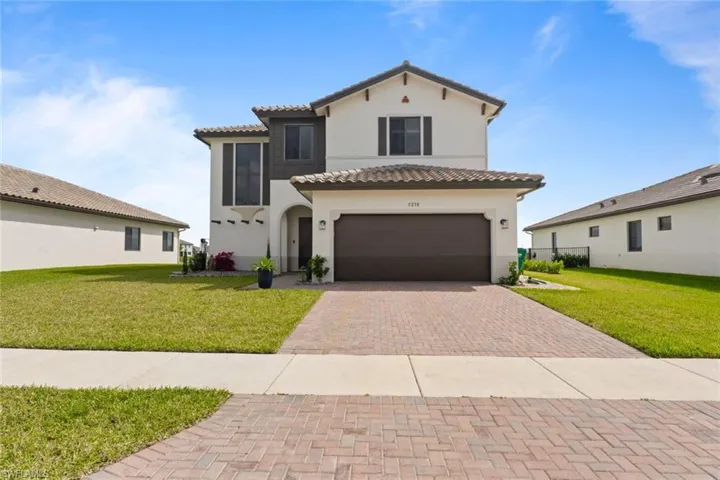 Mediterranean / spanish-style house with an attached garage, a tiled roof, decorative driveway, stucco siding, and a front yard